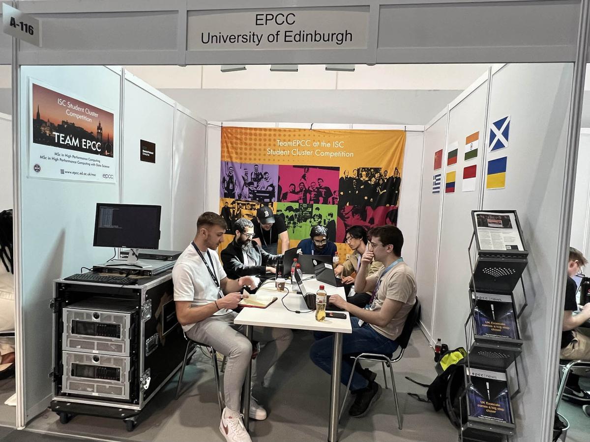 5 young men at a table in a small booth beside a computing cluster