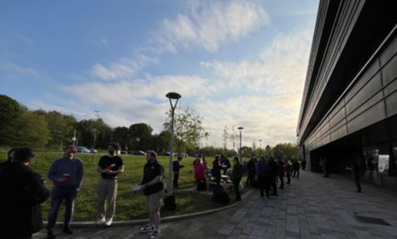 Photo shows queue of people outside modern university building.