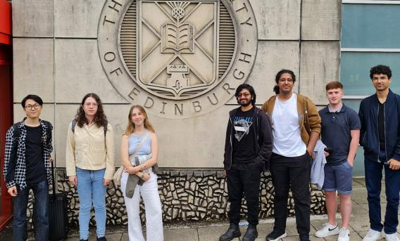 7 undergraduate students standing either side of large University of Edinburgh logo carved into the side of a sandstone building