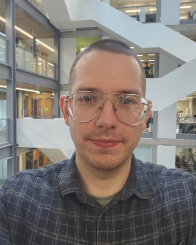 A man with big glasses and short hair, pictured in a modern office building.